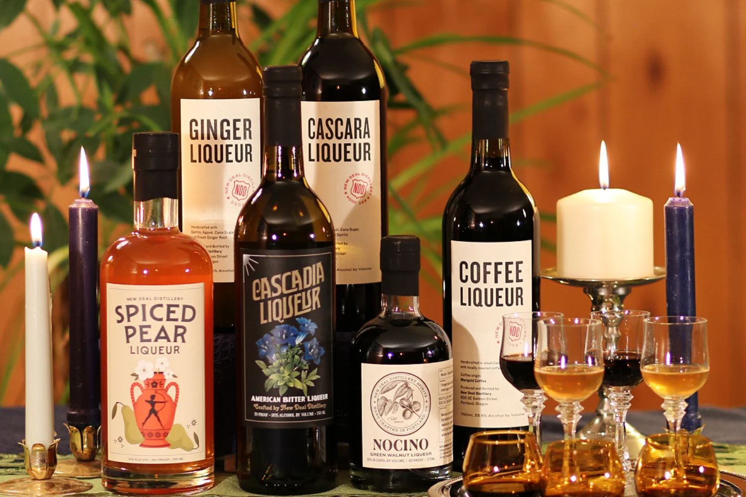 Assorted liqueur bottles and tasting glasses arranged beside lit candles.