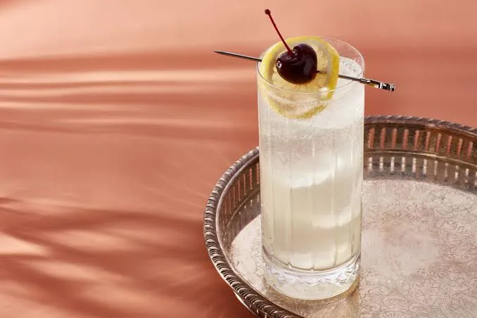 Classic Tom Collins cocktail with lemon twist and cherry garnish.