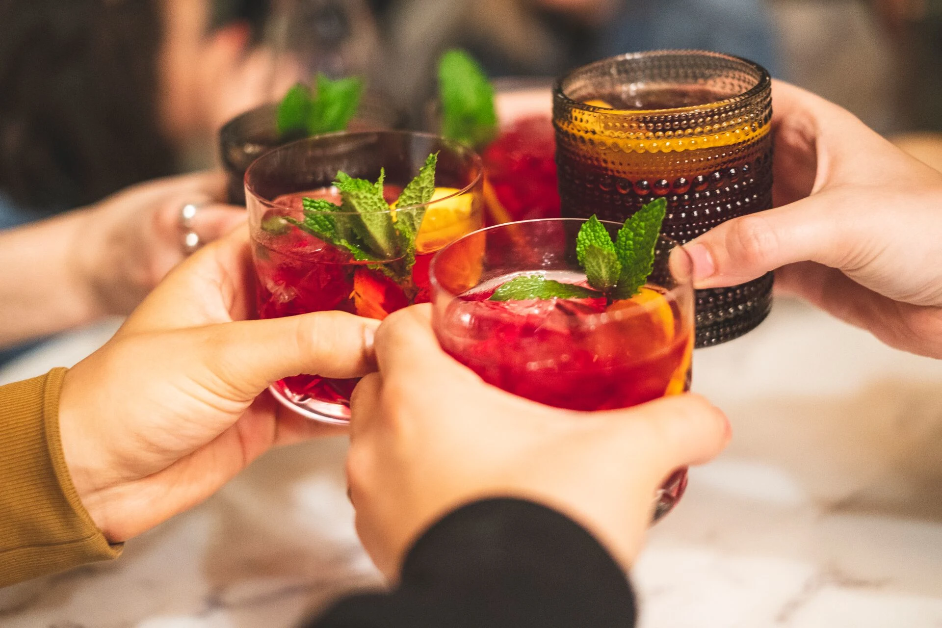 Friends clinking glasses of colorful cocktails with fresh mint at a bar during a social gathering.