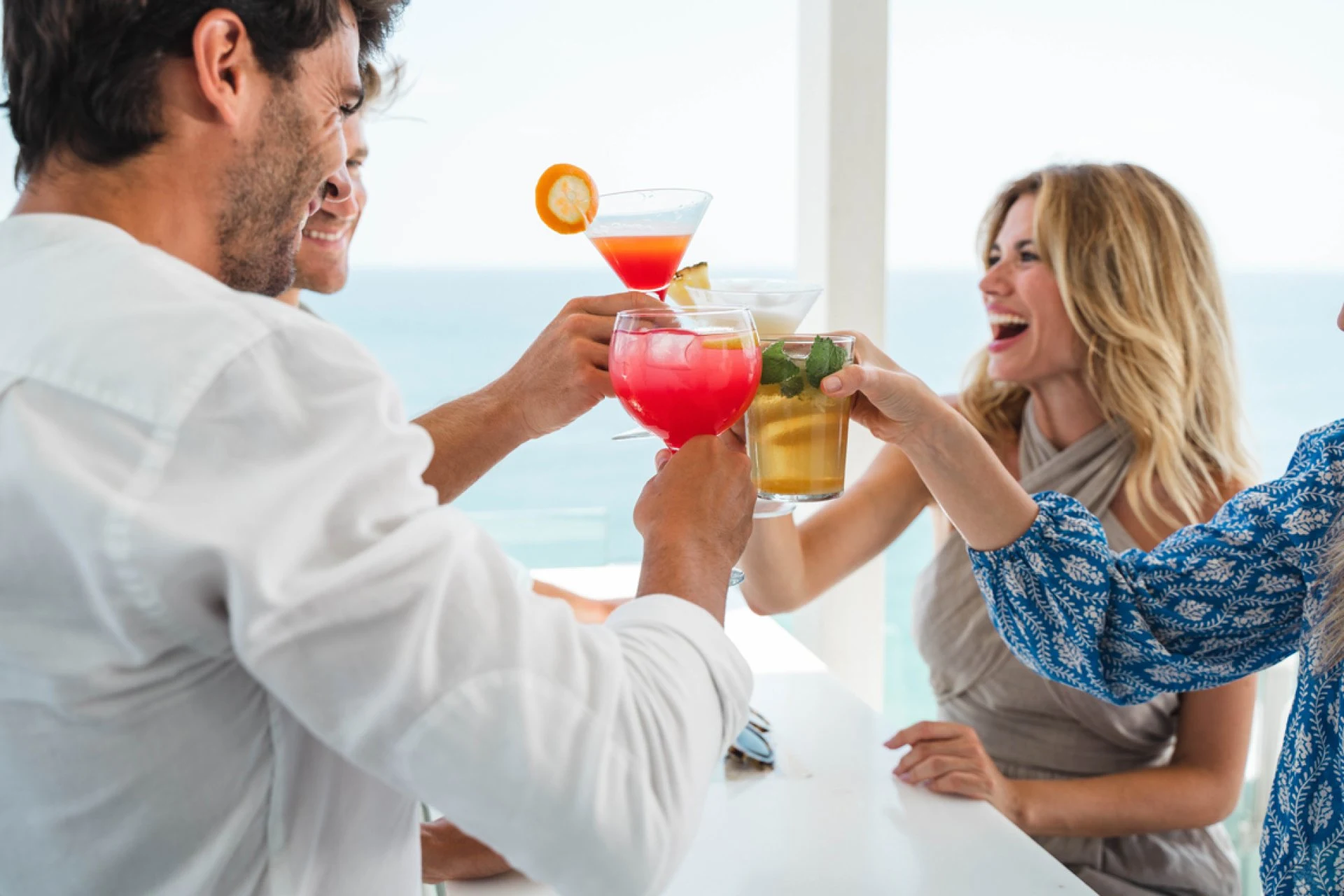 Friends toasting with cocktails at a seaside restaurant.