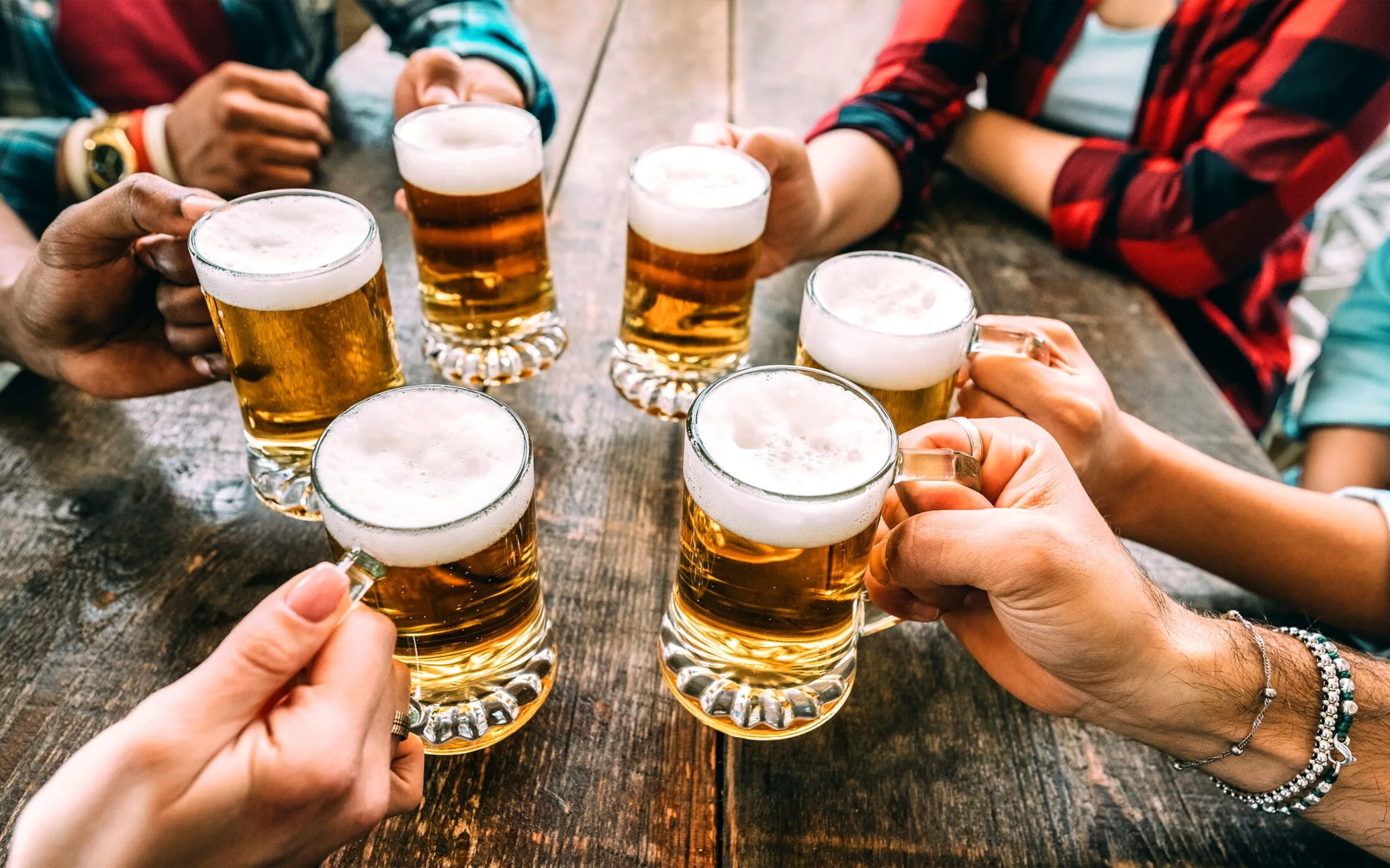 Group of friends raising beer glasses together at a table during a social gathering.