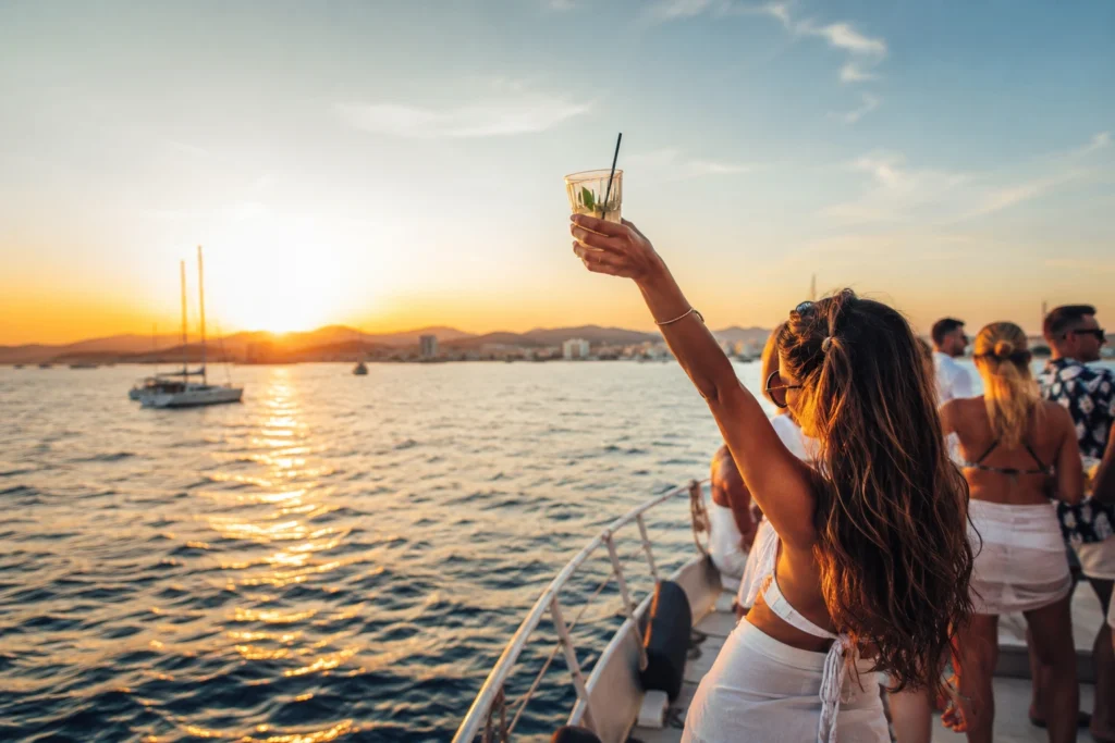 Ibiza boat party at sunset with guests enjoying drinks on the sea.