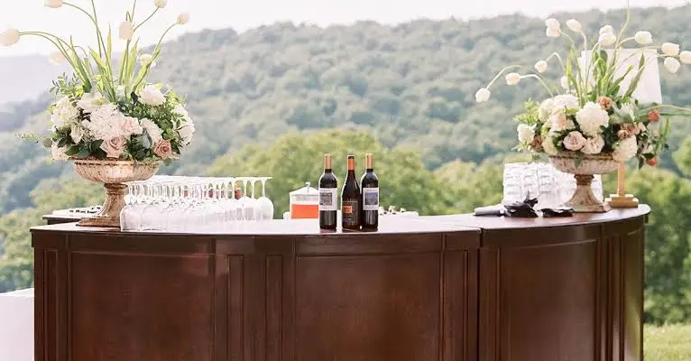 Luxury outdoor wedding bar setup with flowers, glasses, and wine bottles.
