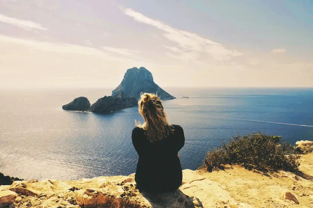 Person overlooking Ibiza’s coastline and Es Vedrà from a cliff.