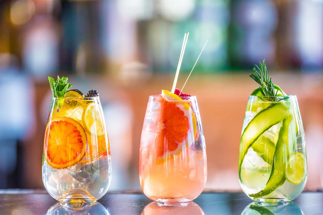 Three colorful cocktails with fresh fruit and herb garnishes.