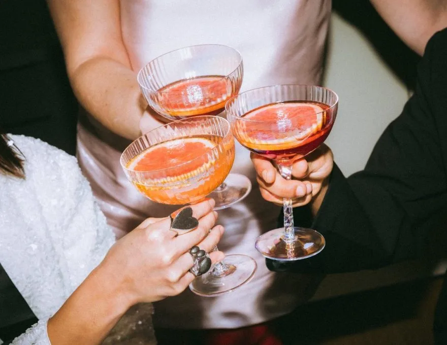 Three people toasting with elegant pink cocktails in coupe glasses.