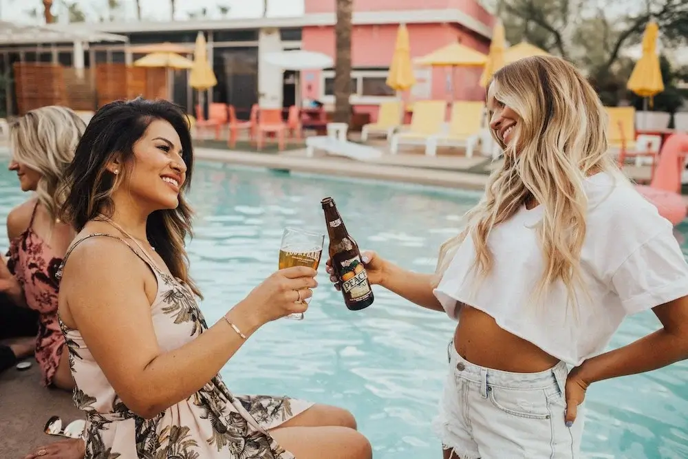 Two friends enjoying beer by a swimming pool during a sunny outdoor gathering in Spain.
