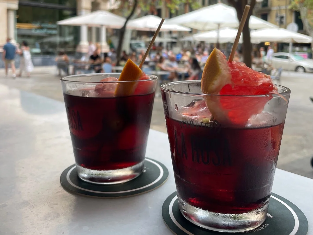 Two red vermouth cocktails with citrus garnish on an outdoor cafe table.