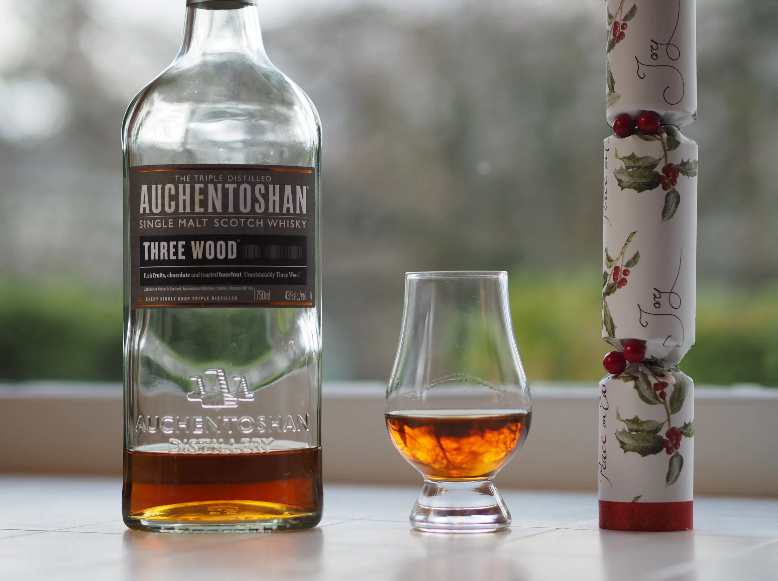 Auchentoshan Three Wood whisky bottle beside a tasting glass.
