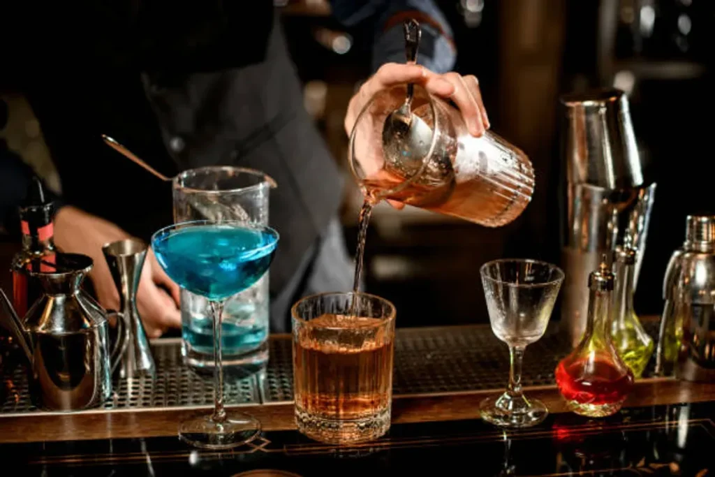 Bartender mixing colorful cocktails with shakers and glasses at a bar.
