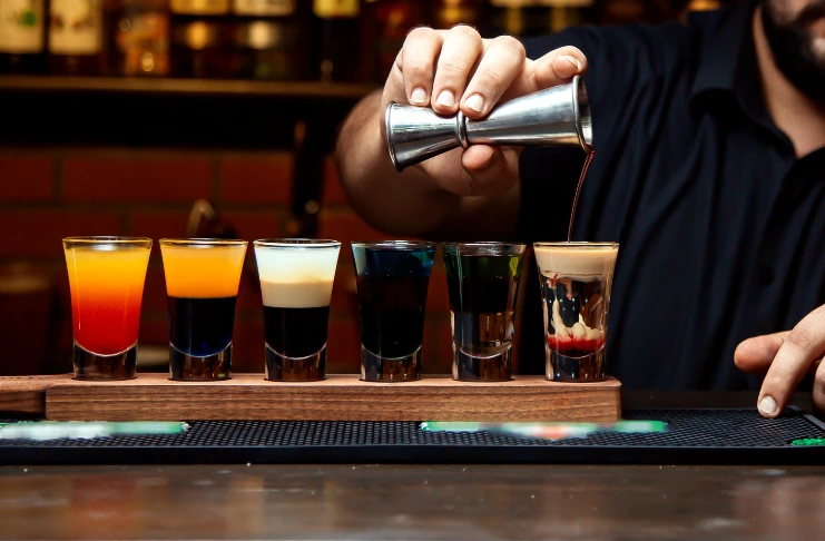 Bartender pouring colorful shots into glasses on a bar counter