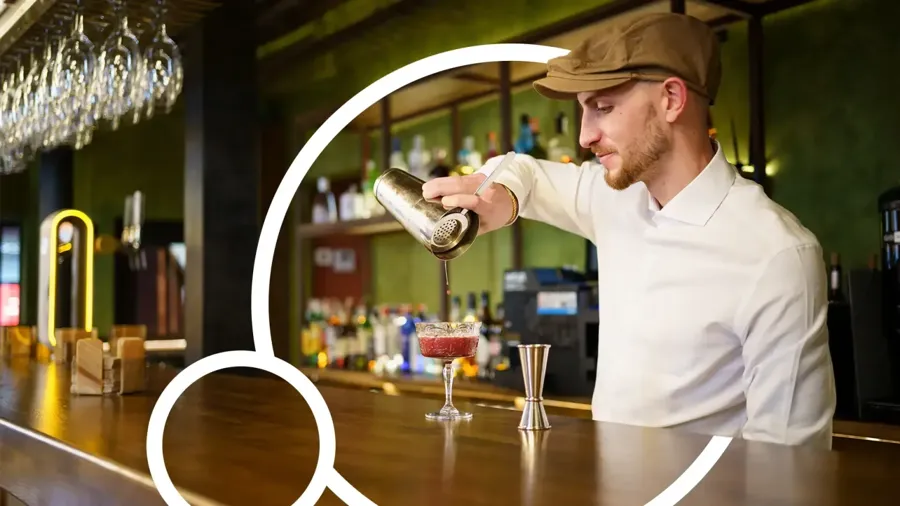 Bartender preparing a cocktail with a shaker behind a bar counter.