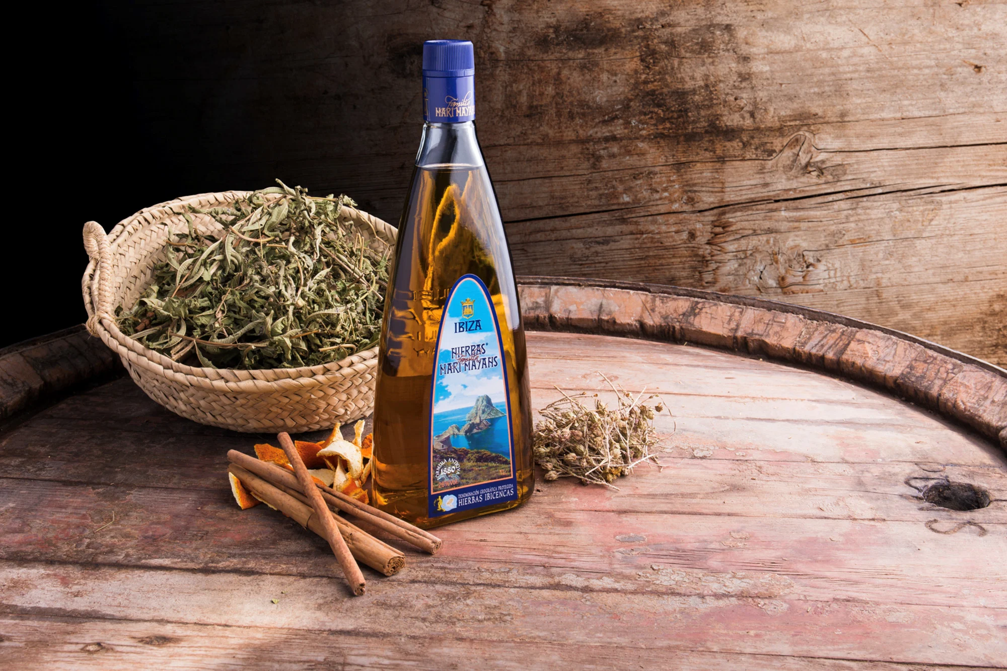 Bottle of Hierbas liqueur with herbs, cinnamon, and spices on a wooden surface.