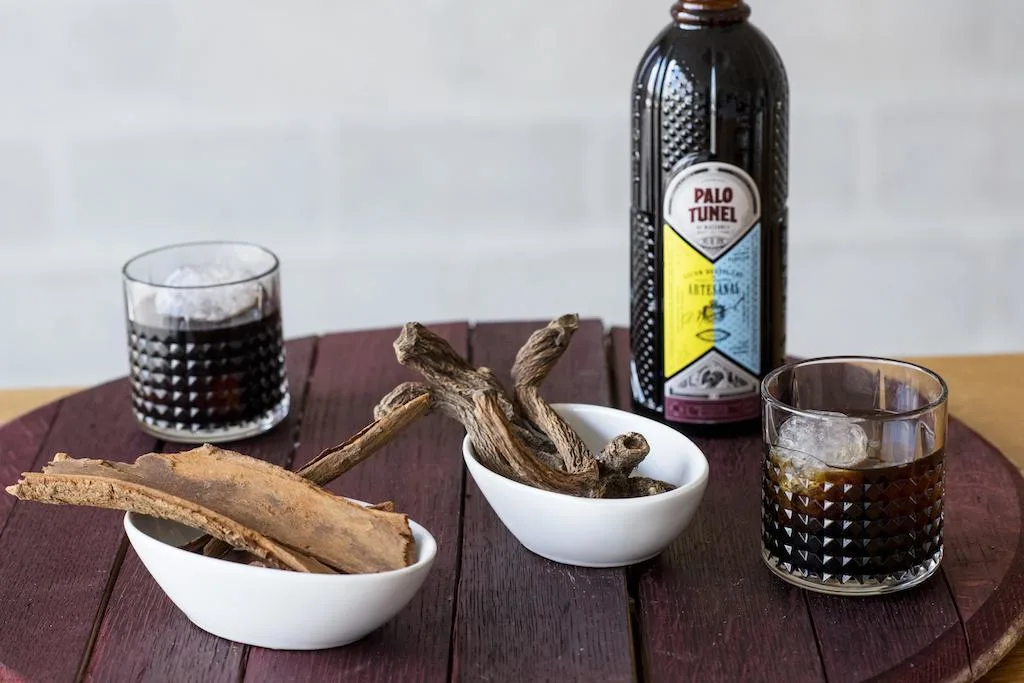 Bottle of Palo liqueur with glasses and herbal ingredients on a table.