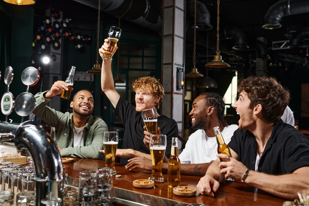 Friends celebrating a bachelor party with beers and a cheerful toast at a bar.