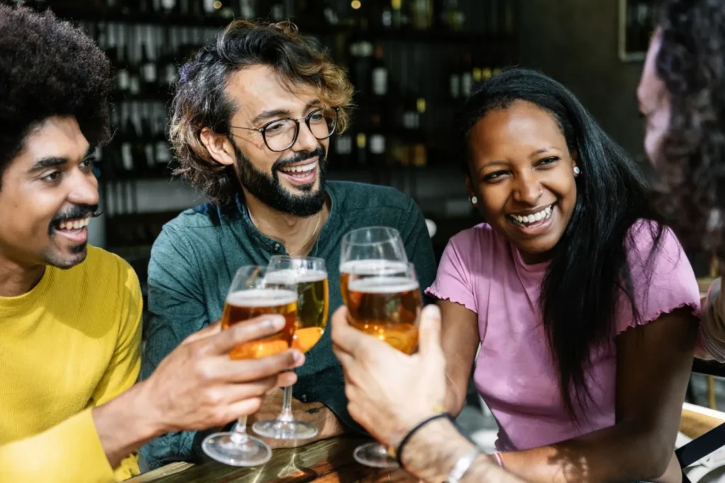 Friends laughing and raising glasses of beer together at a bar.