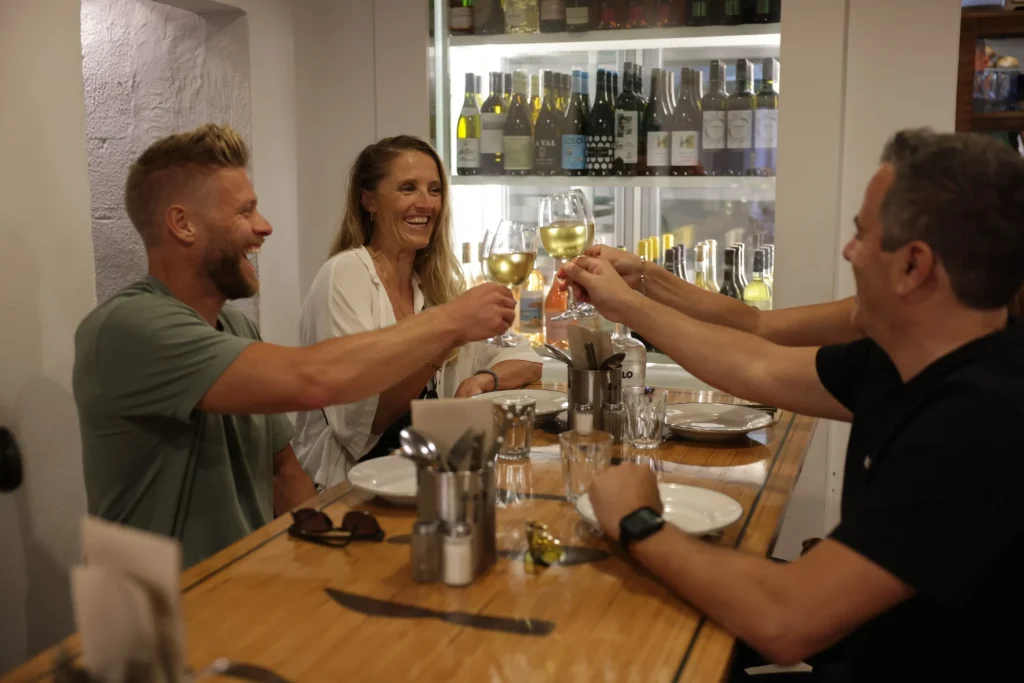 Friends smiling and toasting with glasses of white wine at a restaurant table.