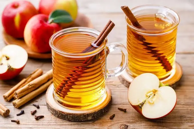 Glass mugs of hot apple cider with cinnamon sticks and apples.