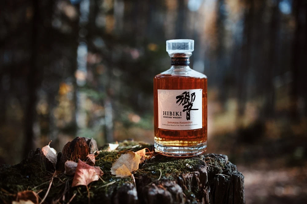 Hibiki Japanese Harmony whisky bottle in a woodland setting.