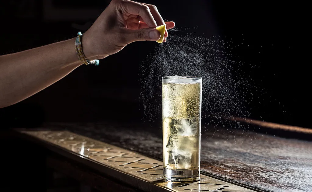 Highball cocktail with lemon garnish at a bar.
