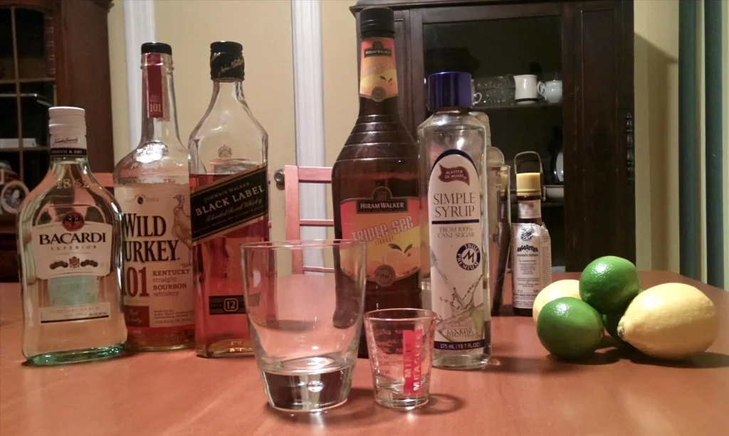 Home bar setup with liquor bottles, cocktail ingredients, limes, lemons, and mixing tools.