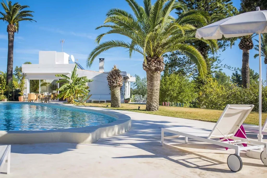 Luxury Ibiza villa with a swimming pool, palm trees, and outdoor lounge chairs.