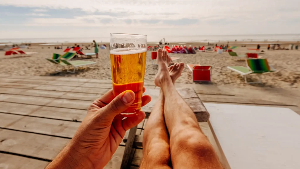 Person relaxing on a beach while holding a glass of beer.