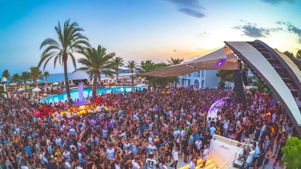 Scenic Ibiza beach with clear blue water, sun loungers, umbrellas, and rocky island views.