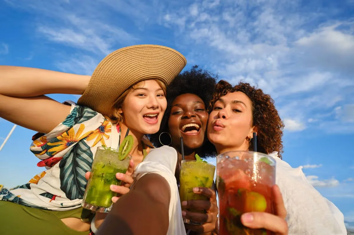 Three friends enjoying colorful cocktails outdoors on a sunny day.