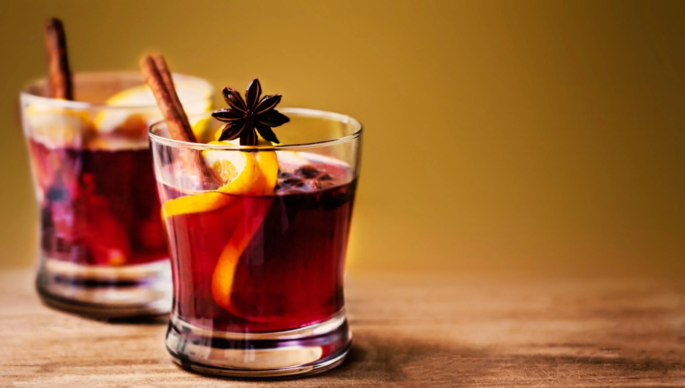 Two glasses of mulled wine with cinnamon and orange garnish.