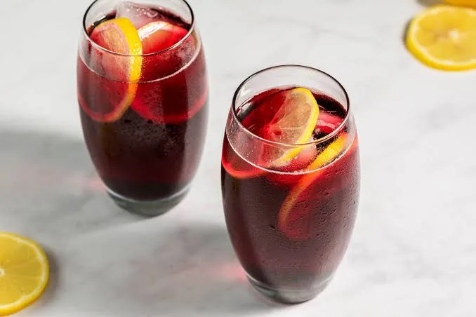 Two glasses of red sangria with lemon slices on a marble surface.