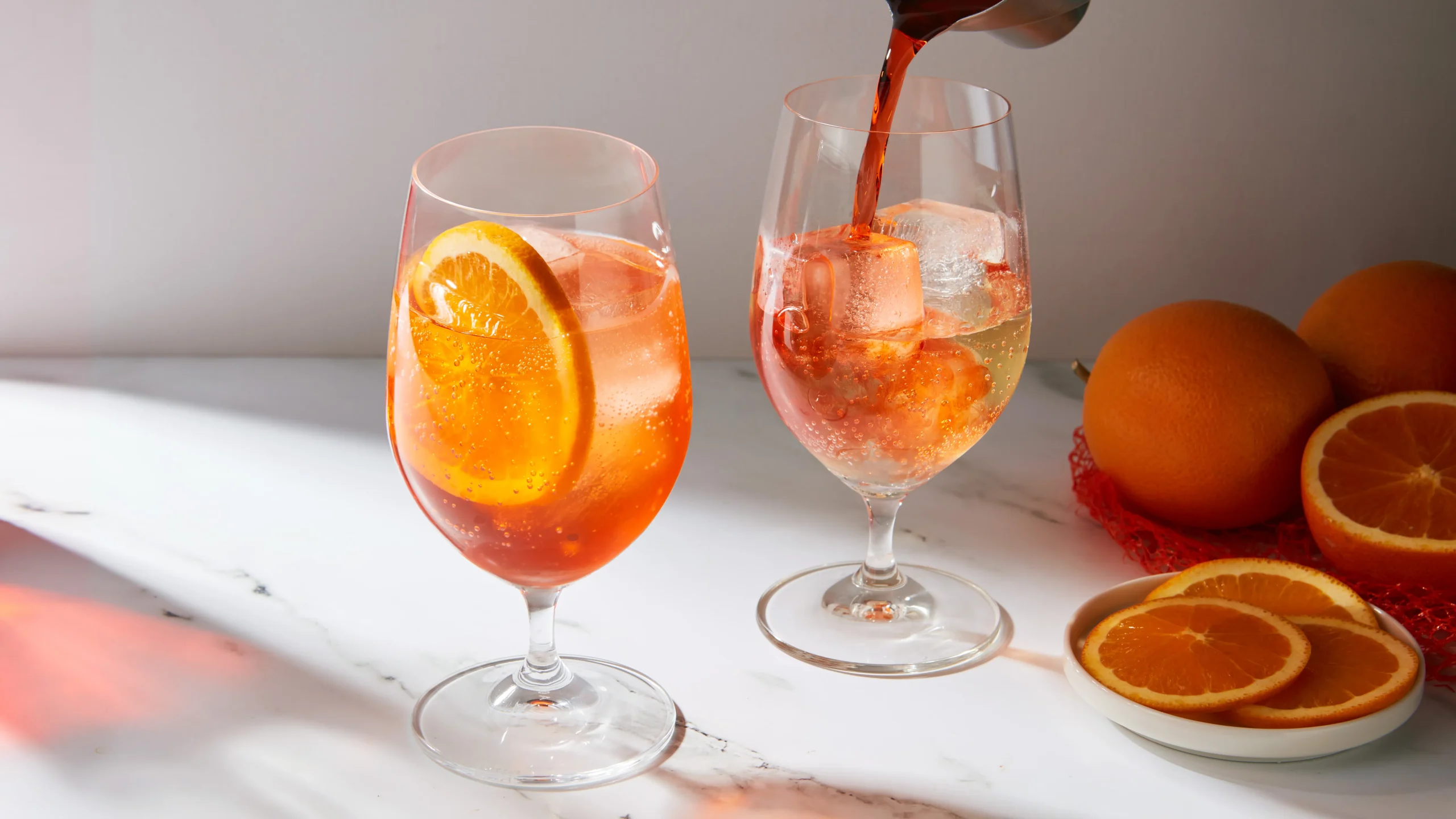 Two orange spritz cocktails with ice and citrus slices on a white table.