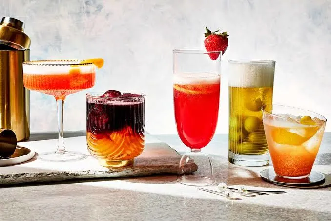 Assorted colorful cocktails in glasses with garnishes on a bar counter.