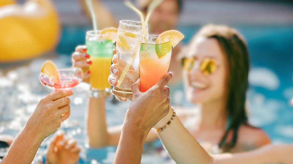 Friends toasting with colorful cocktails by the pool.