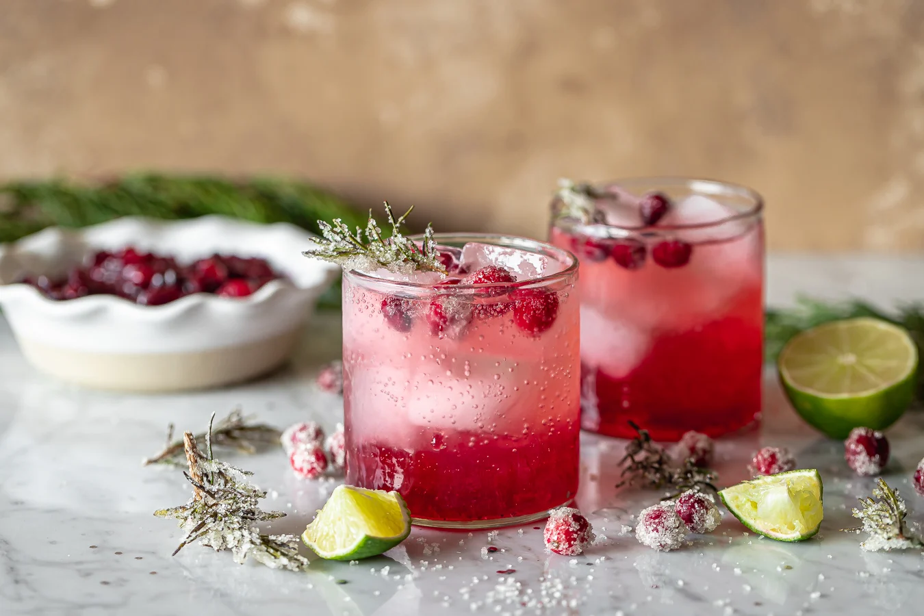 Festive cranberry Christmas drinks with lime, ice, and sugared rosemary.